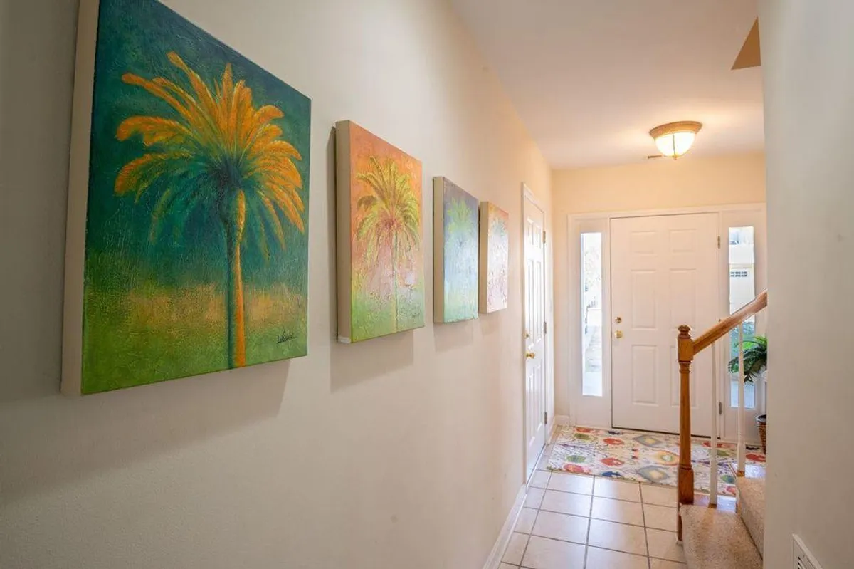 This image captures the home's front door, staircase, and eye-catching palm tree paintings. The scene suggests an inviting entryway, with vibrant, nature-inspired art and a sense of anticipation as guests arrive or depart for outdoor activities.