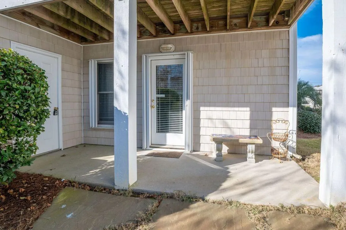 A welcoming exterior shot of the property’s front door framed by columns, a bench, and neatly kept bushes. The front porch area looks inviting, with space to sit and relax, creating a sense of arrival and connection to the outdoors.