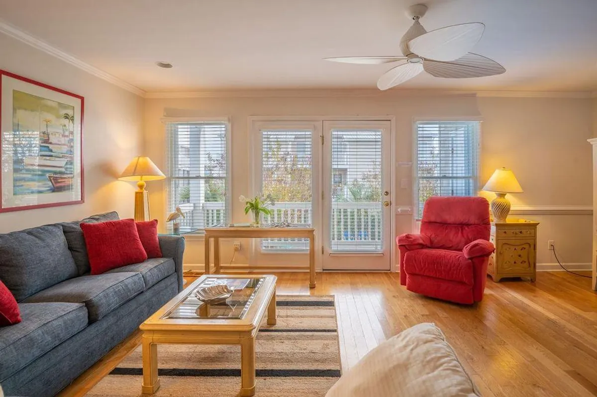 A comfortable basement lounge area featuring a sofa, red chair, coffee table, and a standing lamp. The room's arrangement is ideal for group gatherings, casual lounging, or movie nights, offering a welcoming and flexible layout.