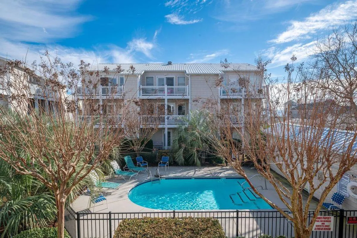 A sparkling swimming pool is surrounded by lush landscaping and poolside chairs, with balconies overlooking the area. The tranquil setting invites relaxation and social gatherings under the sun.