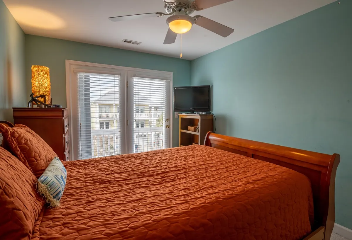 This image features a cozy bedroom with a bed adorned with an orange quilt, wooden furniture, and sliding glass doors that open to an outdoor area. The doors allow natural light to filter in and suggest easy access to a private balcony or deck, supporting a seamless transition between indoor relaxation and outdoor enjoyment.