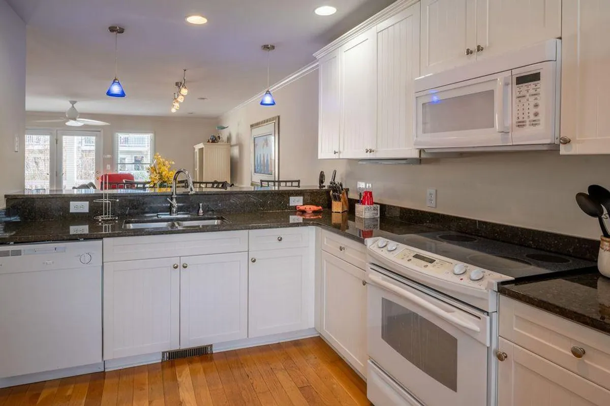 A spacious, modern kitchen featuring granite countertops, white cabinetry, stainless steel appliances, and striking blue pendant lights. The layout encourages gathering, with ample room for meal prep and casual conversations.